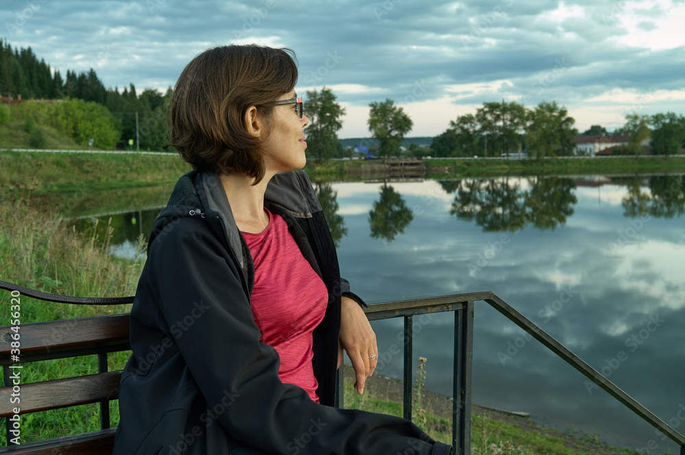 Fototapeta premium Young beautiful woman sitting on bench and looking at lake