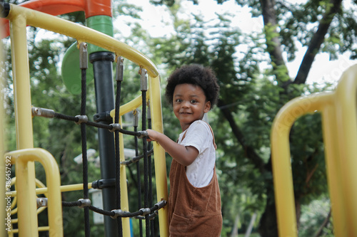 Active African little boy afro hair enjoy playing outdoors, 3 Years kid having fun climbing rope on playground in the park on a sunny day, side view