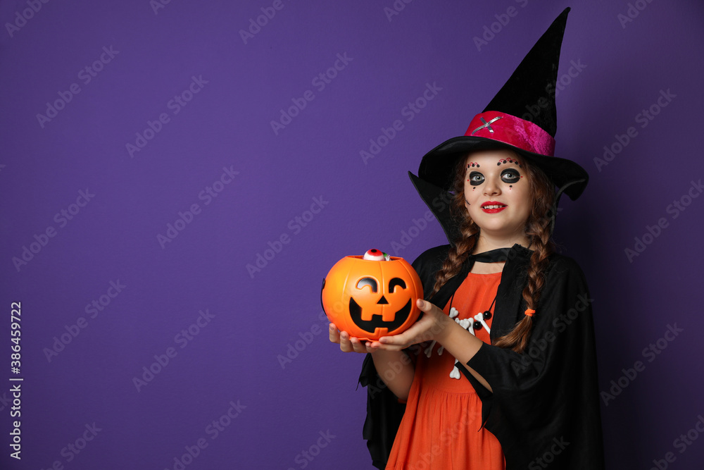 Cute little girl with pumpkin candy bucket wearing Halloween costume on purple background. Space for text Cute little girl with pumpkin candy bucket wearing Halloween costume on purple background. Space for text