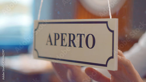Close up of staff turning aperto sign hanging on glass door in italian restaurant. photo