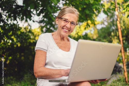 Happy senior old woman working online with laptop computer outdoor in garden