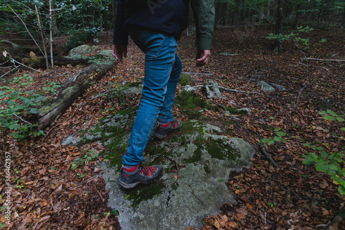 Young man wearing mountain hiking boots, blue jeans and green jacket, walking in the woods during fall season