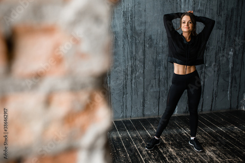 Caucasian girl in sportswear stands against the background of a gray wall in a loft studio. Sport and warm up