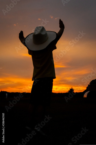 Sunset silhouette of cowboy with hat and hands raised