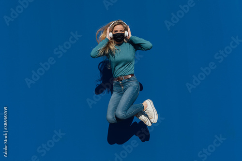 Young woman jumping for joy while listening to music and wearing her protective mask Concept of happiness and security.