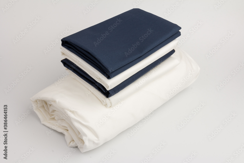 Stack of clean white and blue bed sheets on white background, closeup. Stack of clean white and blue bed sheets on white background, closeup.