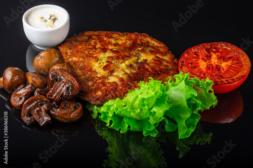 Potato pancakes with lettuce leaves, fried mushrooms, grill vegetables and blue cheese sauce. Black background.  Close up. Selective focus.