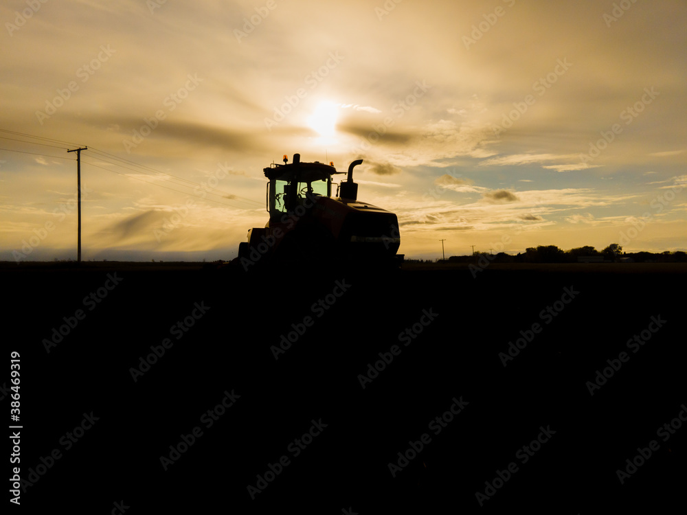 Fototapeta premium Tractor Silhouette in Field at Sunset in North Dakota.