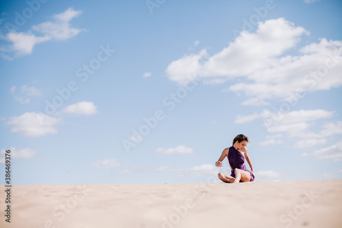 A young, slender girl in a beige dress with purple cloth in her hands posing in the desert in the wind © Denis