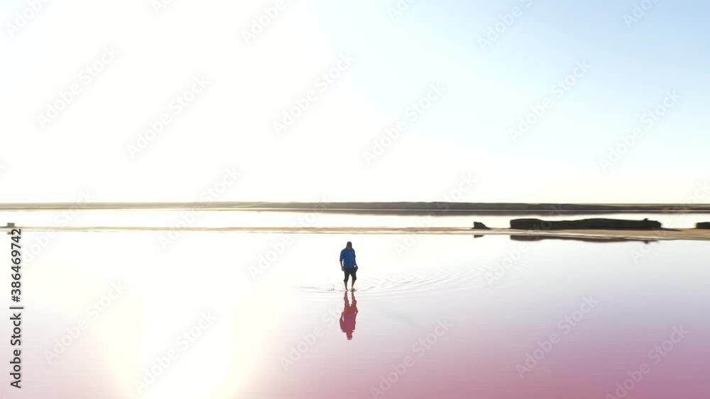 Lonely man in blue jacked in pink lake water under clear blue sky in summer day. UHD 4k drone video Lonely man in blue jacked in pink lake water under clear blue sky in summer day. UHD 4k drone video