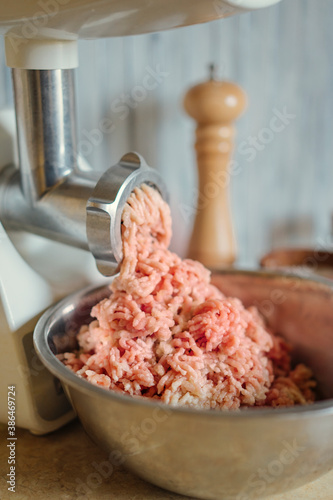 Mincer machine with fresh chopped meat at home kitchen. Meat grinder. Natural day light. Organic meat. Minced meat is wound and lies in a metal bowl. Copy space, selective focus.