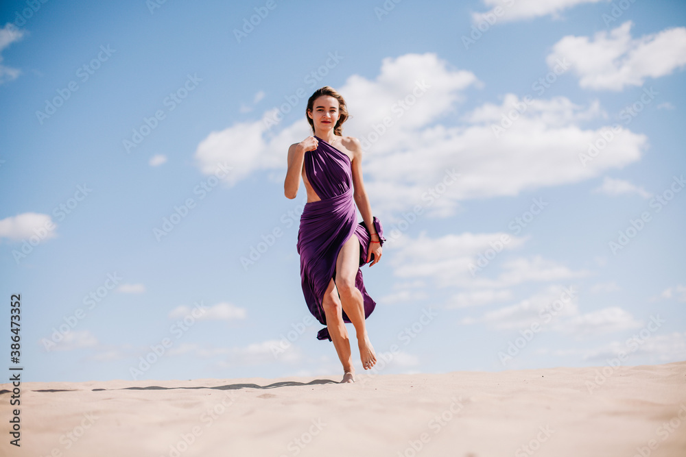 A young, slender girl in a beige dress with purple cloth in her hands posing in the desert in the wind A young, slender girl in a beige dress with purple cloth in her hands posing in the desert in the wind
