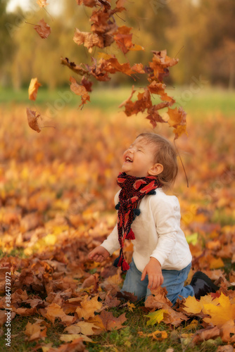 Laughing child playing with maple leaves in autumn park