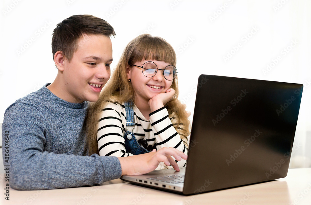 Two smiling children with a laptop communicate with friends on the Internet Brother and sister, technology and home concept. Distance communication on the Internet.