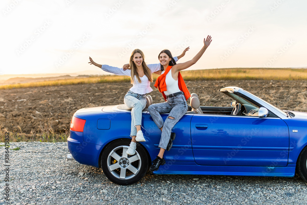 Fototapeta premium Two happy women friends taking selfie when road trip in convertible car.