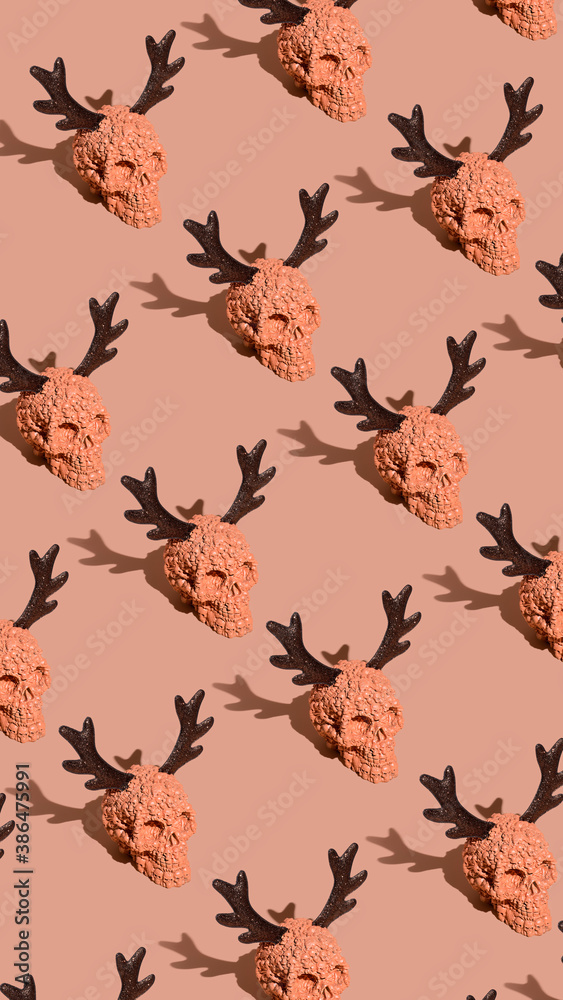 Halloween pattern made with orange skulls with elk antlers on pastel background. Heavy trendy shadows. Contemporary horror aesthetic. Flat lay.