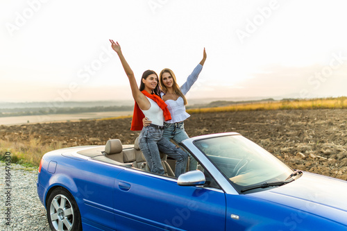 Happy two women in car driving on road trip. Young two women having fun dancing and cheering in car driving on travel vacation together. © F8  \ Suport Ukraine