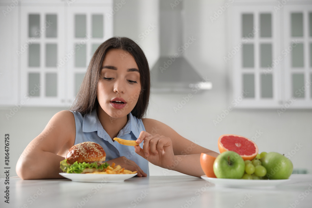 Concept of choice between healthy and junk food. Woman eating French fries in kitchen Concept of choice between healthy and junk food. Woman eating French fries in kitchen