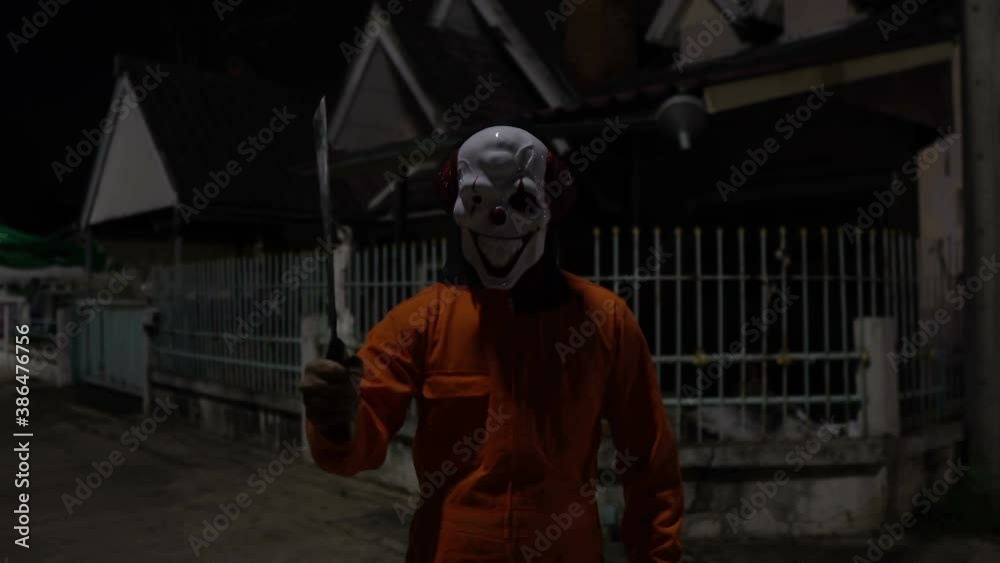 Asian handsome man wear clown mask with weapon at the night scene,Halloween festival concept,Horror scary photo of a killer in orange cloth Asian handsome man wear clown mask with weapon at the night scene,Halloween festival concept,Horror scary photo of a killer in orange cloth