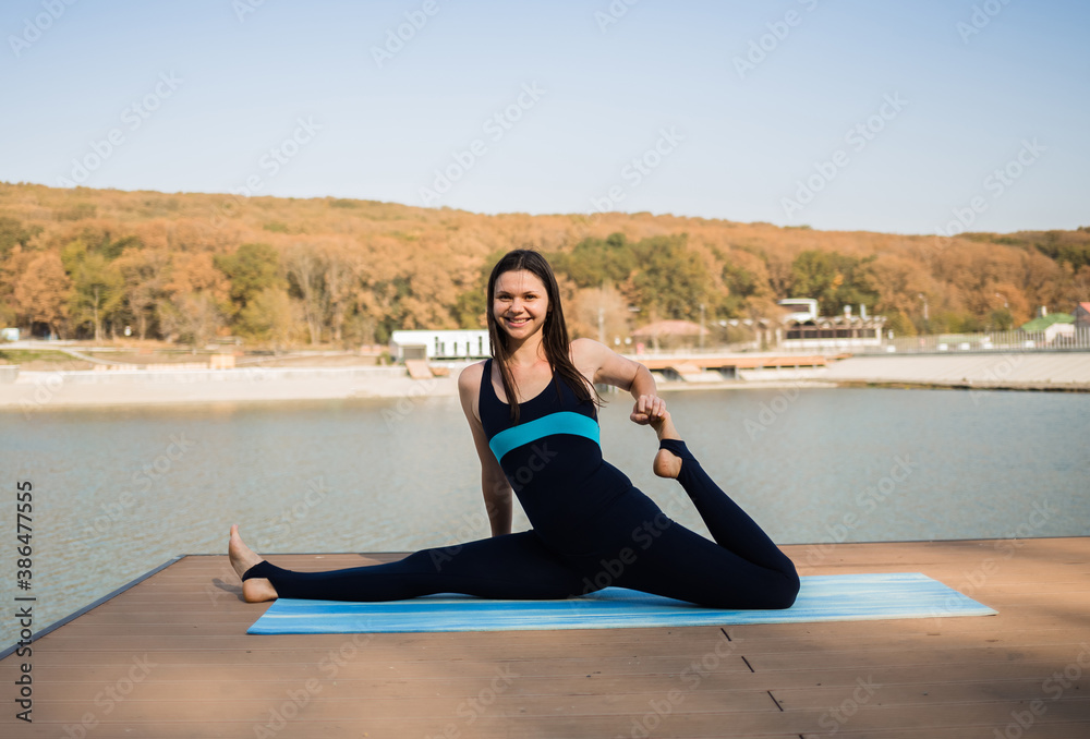 Fototapeta premium a yoga woman stretches on a blue Mat on a pier with a lake background
