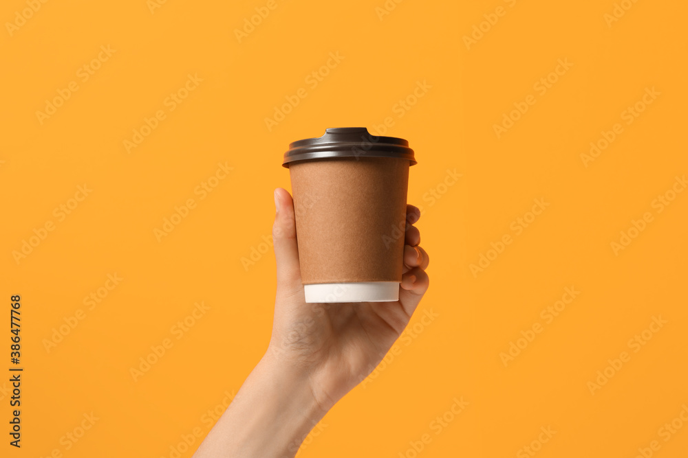Woman holding takeaway paper coffee cup on orange background, closeup - obrazy, fototapety, plakaty 