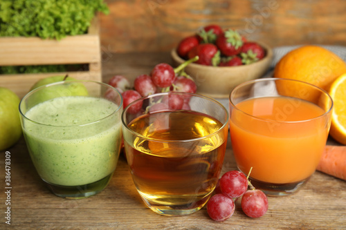 Glasses of delicious juices and fresh fruits on wooden table