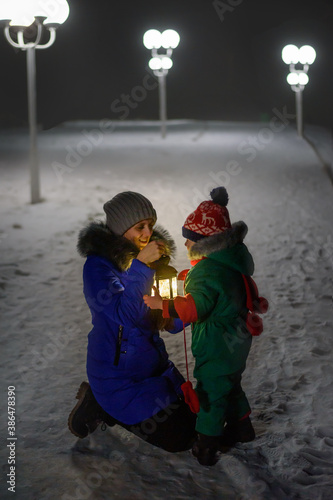 Mother and little son with lantern sitting on the street in winter evening