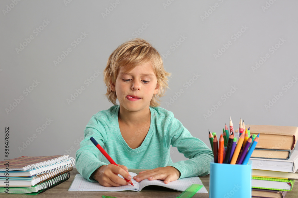 Little boy doing homework at table on grey background