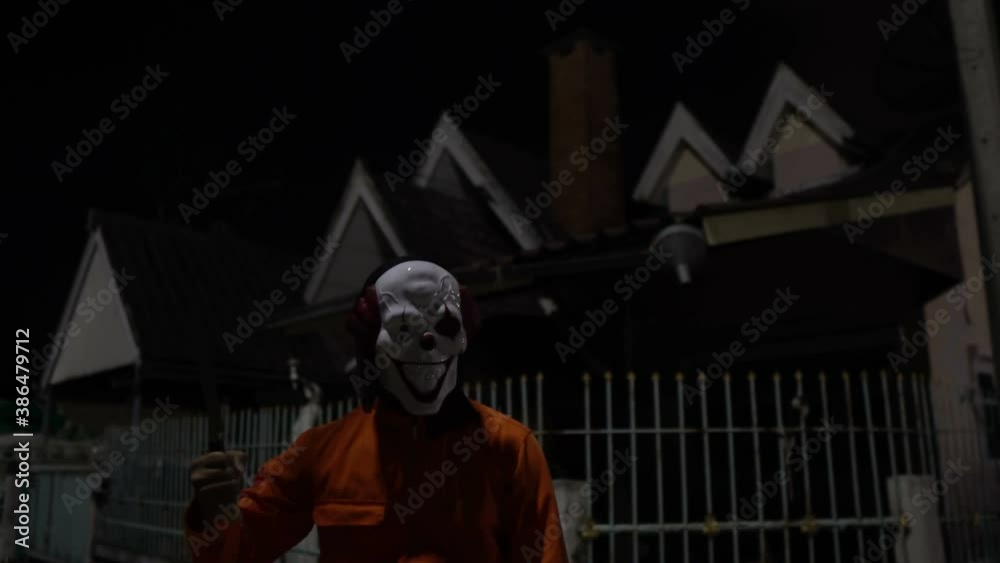 Asian handsome man wear clown mask with weapon at the night scene,Halloween festival concept,Horror scary photo of a killer in orange cloth Asian handsome man wear clown mask with weapon at the night scene,Halloween festival concept,Horror scary photo of a killer in orange cloth