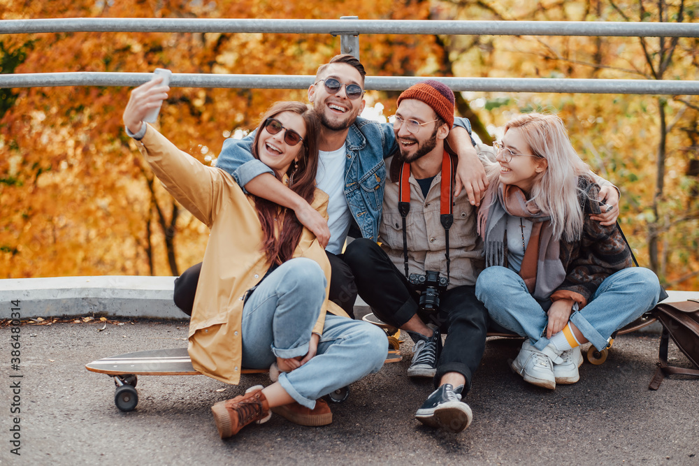 Joyful company of two girls and two boys dressed in autumn casual clothing photographing sitting on skates in public park. Joyful company of two girls and two boys dressed in autumn casual clothing photographing sitting on skates in public park.