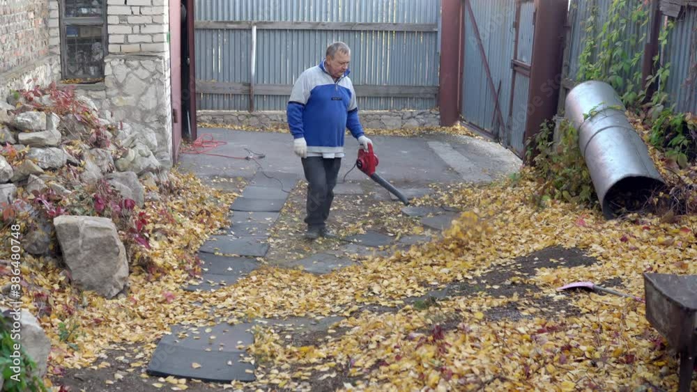 A man blows off fallen leaves in the yard with a blower. Russian yard A man blows off fallen leaves in the yard with a blower. Russian yard