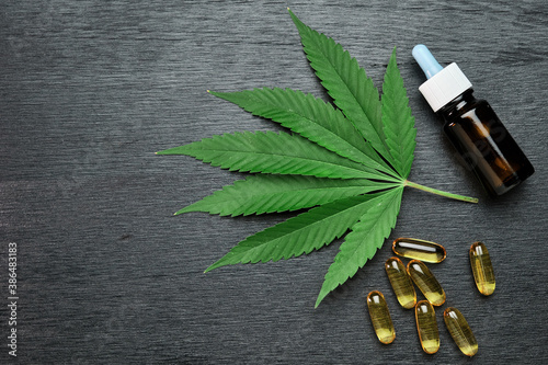 Capsules or pills and bottle with CBD cannabis or hemp oil on the leaf of marijuana on the black wooden background with copy space. Alternative medicine concept. Cosmetics and skin care products