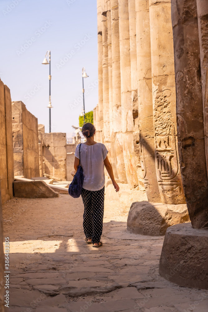 A young tourist in a white t-shirt and hat visiting the temple and looking at the ancient egyptian drawings on the columns of the Luxor Temple, Egypt