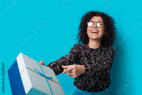 Lovely curly haired woman is smiling at camera and receiving a present on a blue studio wall photo