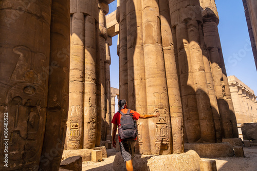 A photographer looking at ancient Egyptian drawings on the columns of the Temple of Luxor, Egypt © unai