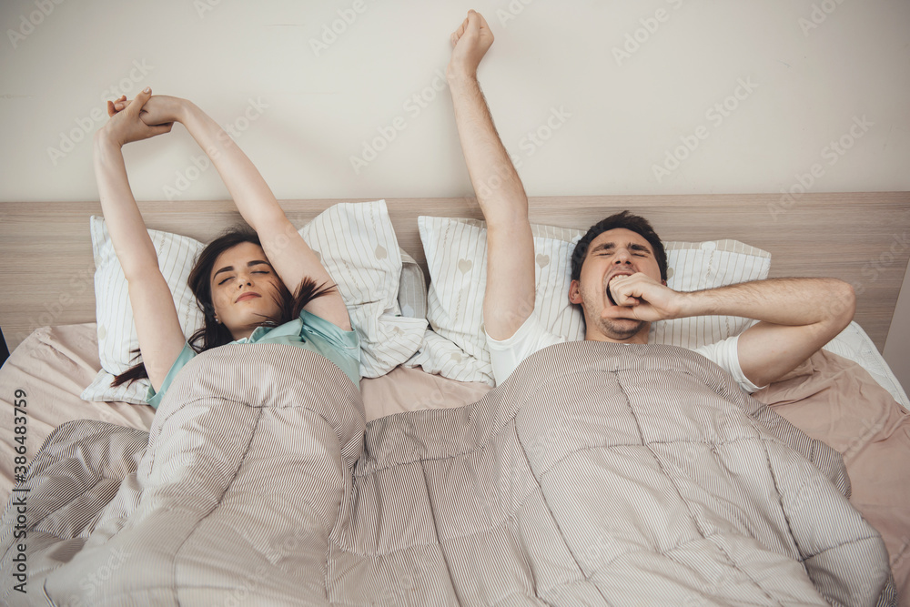 Caucasian couple yawning in bed and stretching in the morning covered with a quilt Caucasian couple yawning in bed and stretching in the morning covered with a quilt