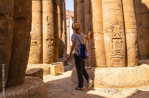 A young tourist in a white t-shirt and hat looking at ancient egyptian drawings on the columns of the Temple of Luxor, Egypt