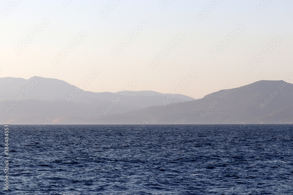 View from the sea to the mountainous islands, coast in the morning. Picturesque seascape, coastline with hills covered by forest in a mist