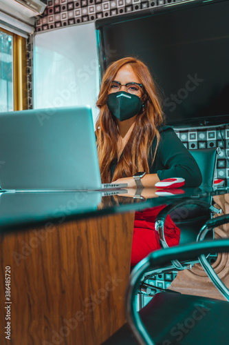 Mujer joven mexicana latina trabajando en oficina de empresa feliz alegre con mascarilla por covid pandemia distanciamiento social precaución photo