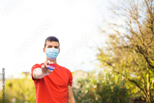 Man with face mask showing I voted today badge at ballot box.