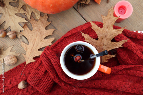 A Cup of hot tea with orange pumpkins, autumn leaves and acorns on a knitted sweater, top view, close-up