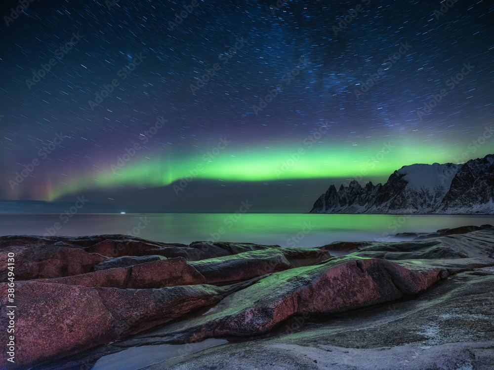 Tungeneset rocks and Aurora Borealis light. Stars trails and northern light. Reflections on the water surface. Senja islands, Norway. Travel - image
