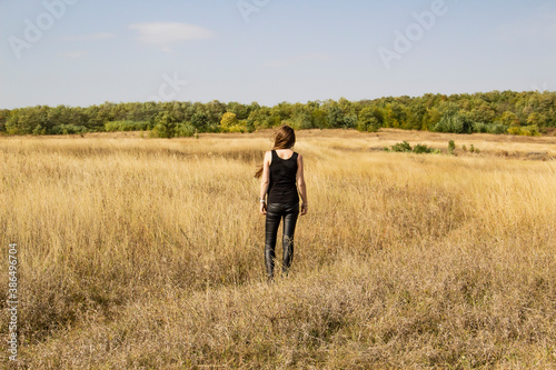 Beautiful young dark haired woman in black clothes stand in field.