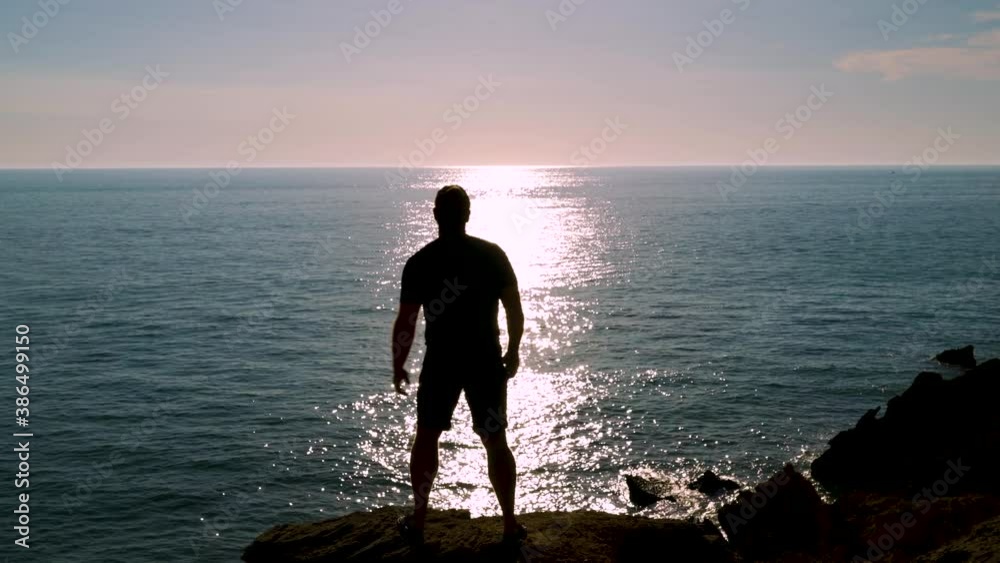 Silueta de hombre en un acantilado frente al reflejo del sol en el mar lavantando los brazos un dáa sensacional. Desde Conil, Cádiz, Andalucía, España, Europa.