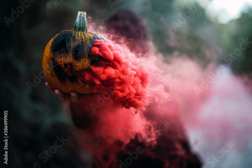 Chico joven con mascarilla por covid 19 con calabaza de halloween con humo de color