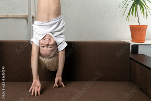 Картината върху платно Boy is upside down over sofa. Funny child hangs upside down.