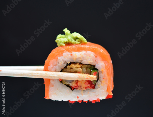 man holding wooden chopsticks sushin, on top of wasabi sushi. dark background.