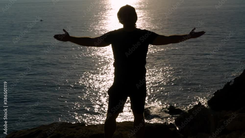 Silueta de hombre en un acantilado frente al reflejo del sol en el mar lavantando los brazos un día sensacional. Desde Conil, Cádiz, Andalucía, España, Europa.