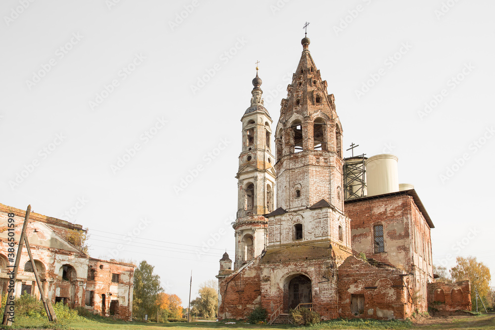 Ruins of a tall bell tower and Russian Orthodox church. Autumn colours, clear sky, no people.