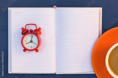 Notes Open Empty Page of Notebook, Red Alarm Clock, Cup of Coffee Latte are on Blue Table – Background, Copy Space, Banner.  Creative Top View Flat Lay Composition. 